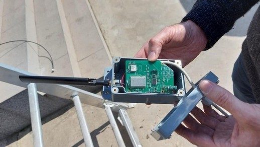 Szenzor elektronikája kézben, a növényház szerkezete előtt