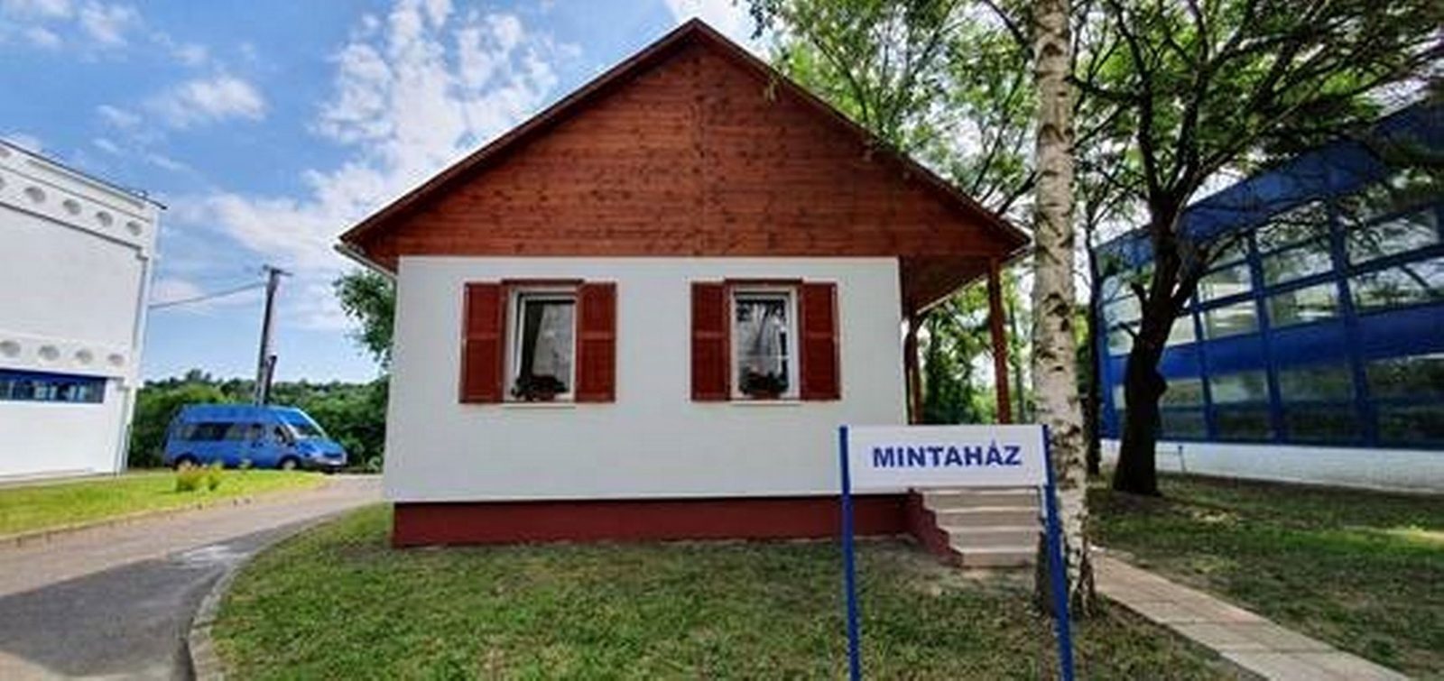 A miskolci mintaház kész oldala piros spalettákkal, előtte Mintaház tábla